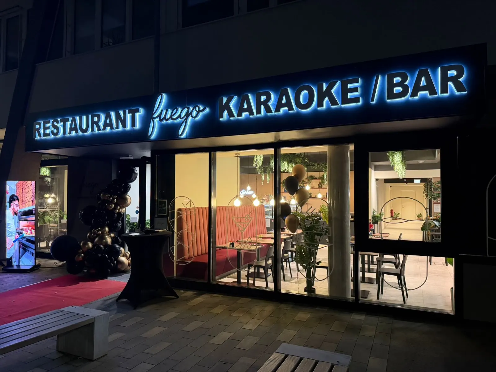 Beleuchteter Eingang des Fuego mit Schriftzug Restaurant Fuego Karaoke / Bar am Abend