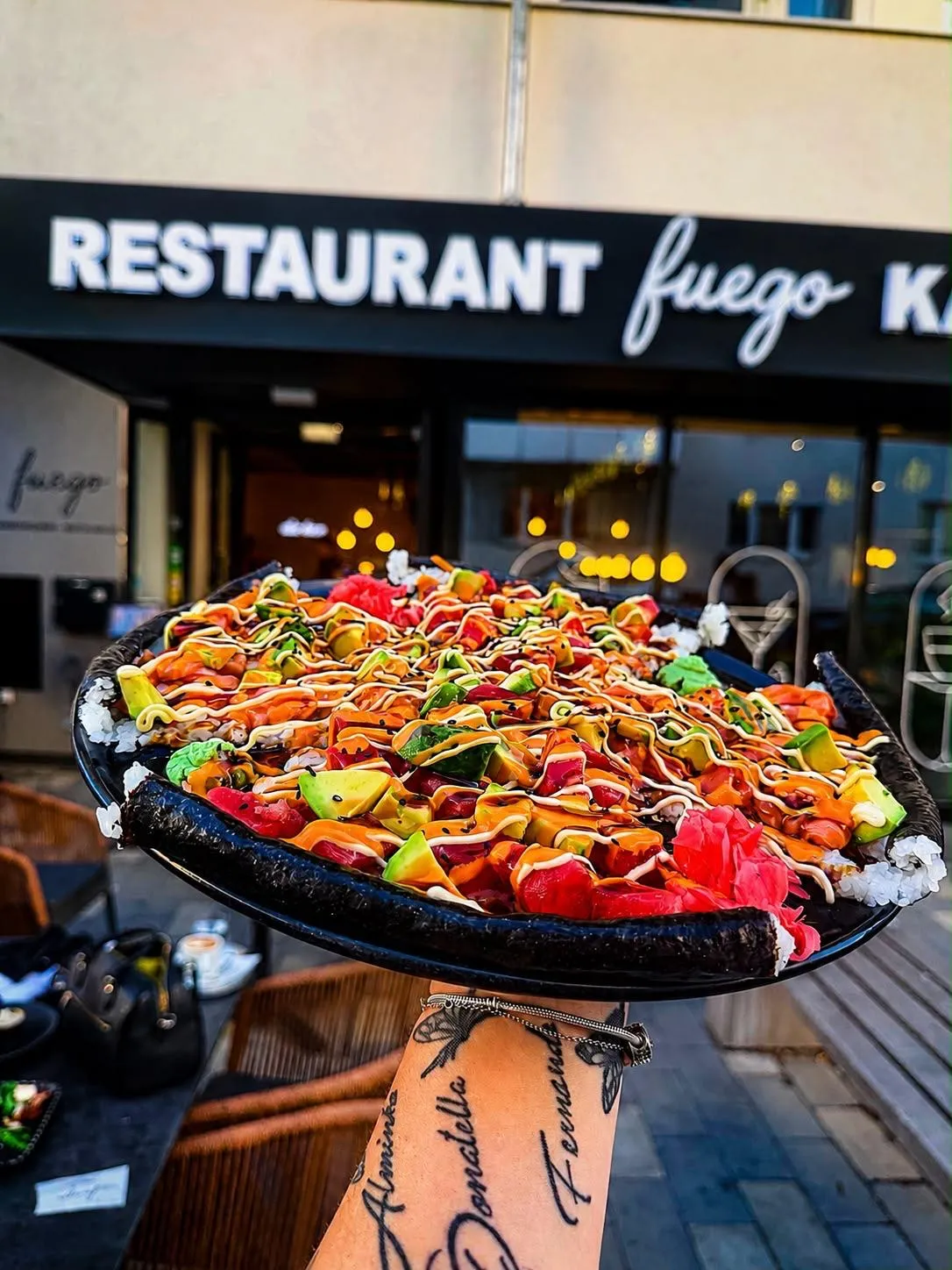 Bunte Sushi-Platte wird vor dem Schriftzug Restaurant Fuego in die Kamera gehalten